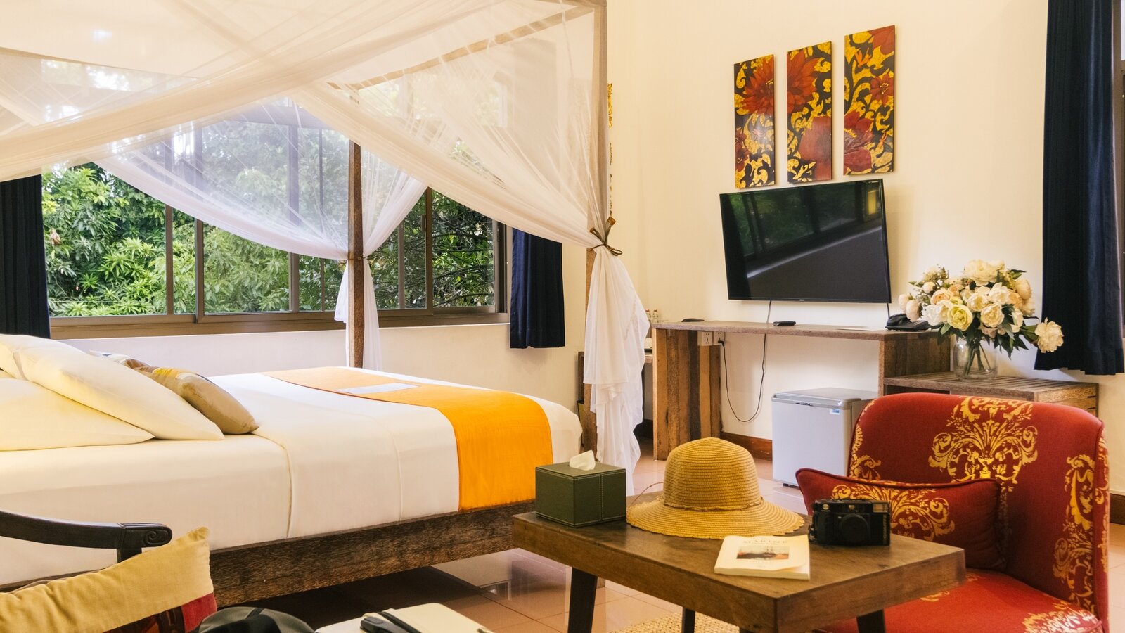 King-size bed with mosquito net, sitting area and garden-facing windows in a Pavilion suite in Phnom Penh