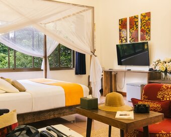 King-size bed with mosquito net, sitting area and garden-facing windows in a Pavilion suite in Phnom Penh