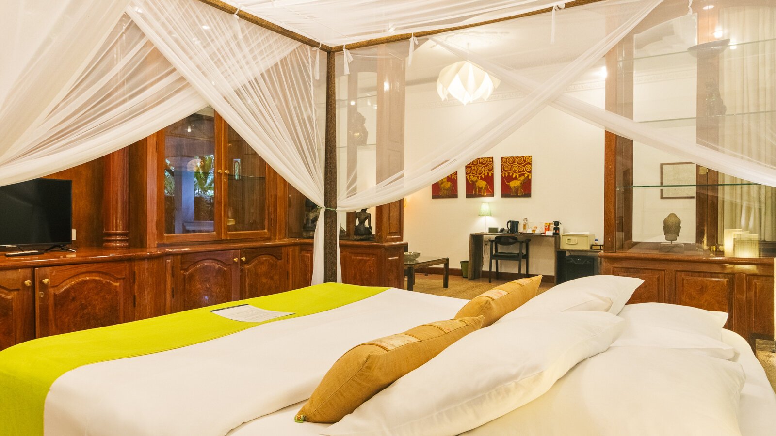 King-size bed with mosquito net, wooden cabinetry and artwork inside a Pavilion Suite in Phnom Penh