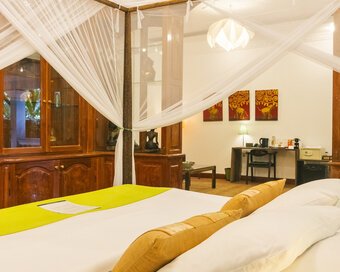 King-size bed with mosquito net, wooden cabinetry and artwork inside a Pavilion Suite in Phnom Penh