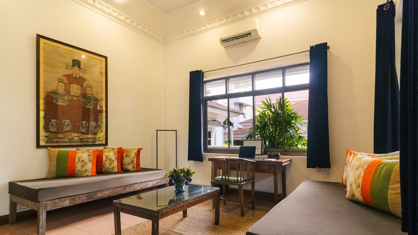 Pavilion Suite living area with day beds, coffee table, writing desk, and Chinese family portrait and garden-facing windows in Phnom Penh