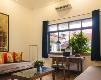 Pavilion Suite living area with day beds, coffee table, writing desk, and Chinese family portrait and garden-facing windows in Phnom Penh