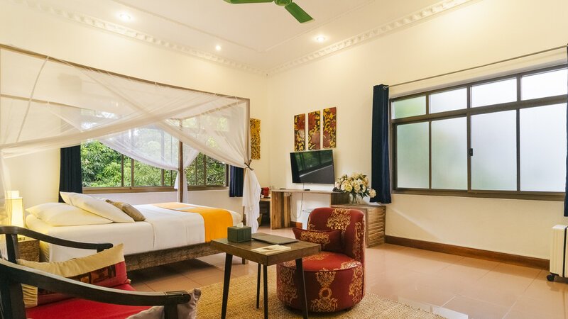 King-size bed with mosquito net, sitting area and garden-facing windows in a Pavilion Suite in Phnom Penh