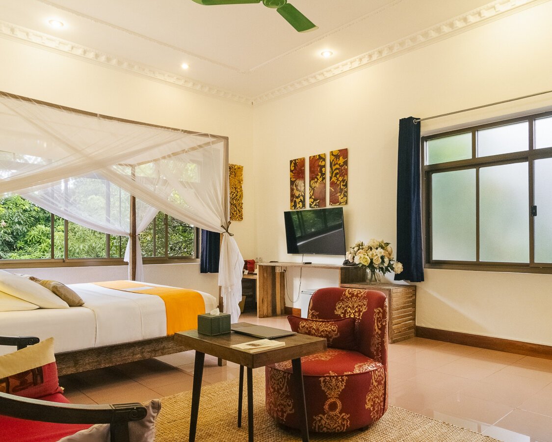 King-size bed with mosquito net, sitting area and garden-facing windows in a Pavilion Suite in Phnom Penh