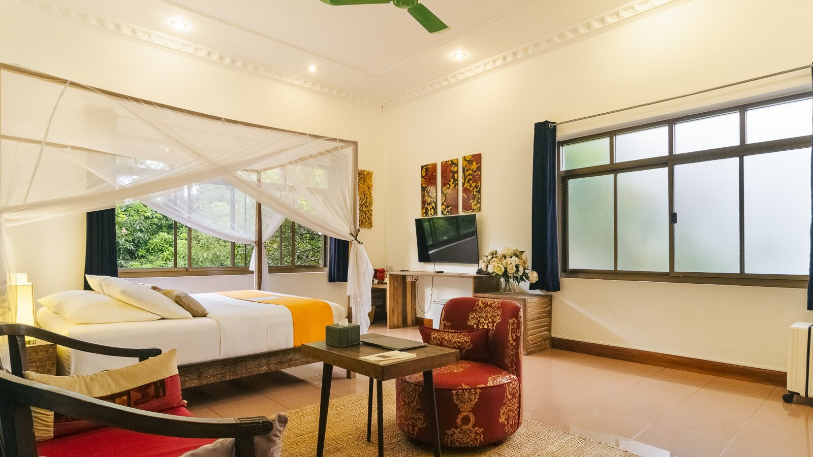 King-size bed with mosquito net, sitting area and garden-facing windows in a Pavilion Suite in Phnom Penh