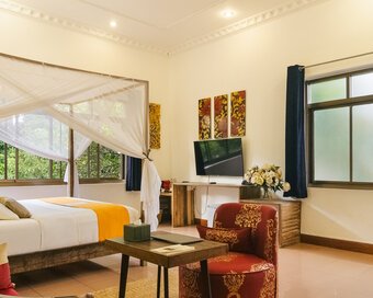 King-size bed with mosquito net, sitting area and garden-facing windows in a Pavilion Suite in Phnom Penh