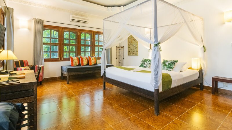 Wide view of a Superior Double Room with king bed, mosquito net, seating and garden-facing windows