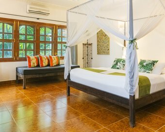 Wide view of a Superior Double Room with king bed, mosquito net, seating and garden-facing windows