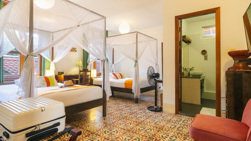 Twin room with two mosquito-net beds, Cambodian patterned tile floor and bathroom entrance at Pavilion Phnom Penh