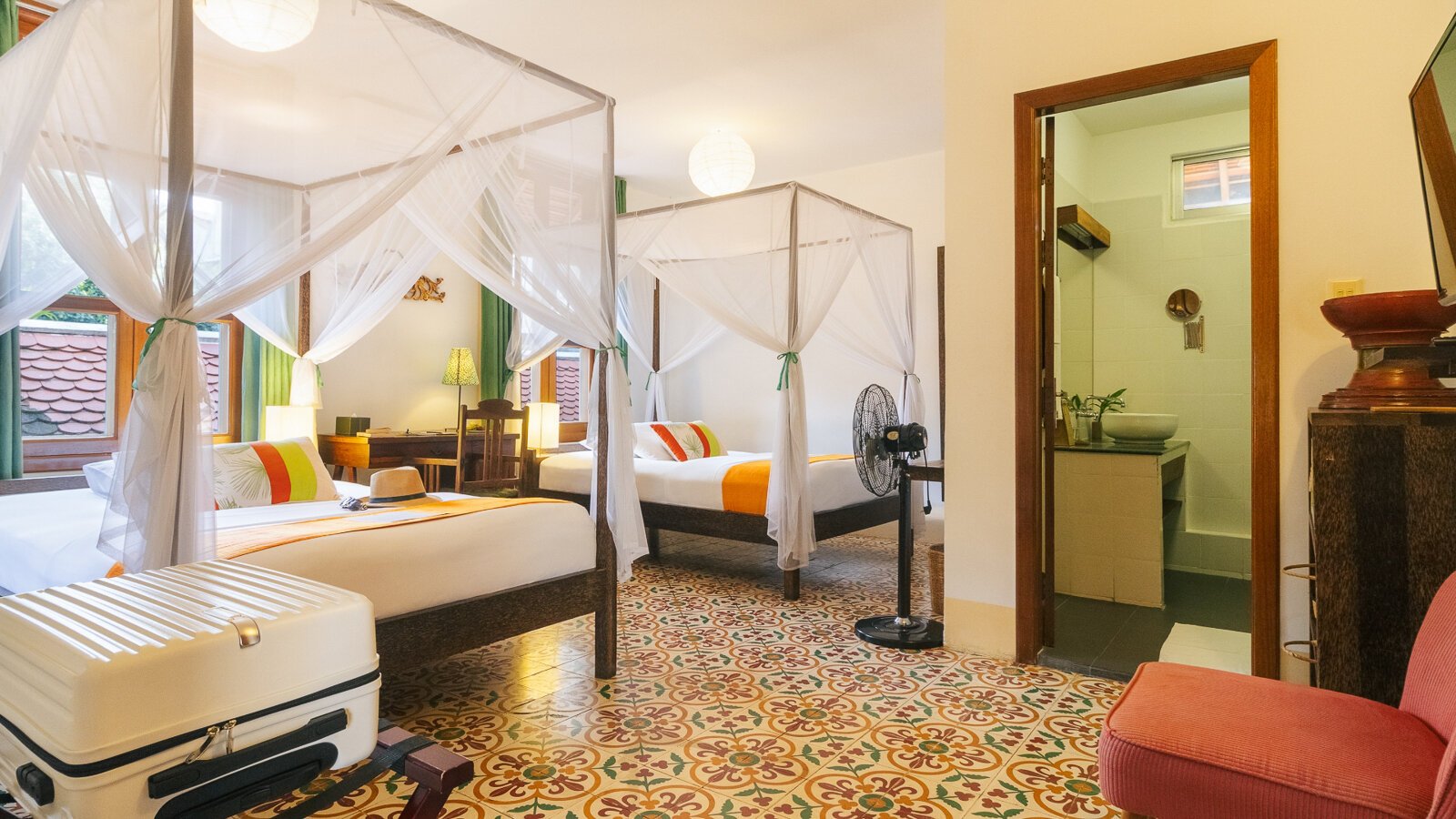 Twin room with two mosquito-net beds, Cambodian patterned tile floor and bathroom entrance at Pavilion Phnom Penh