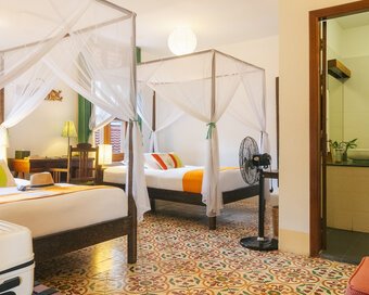 Twin room with two mosquito-net beds, Cambodian patterned tile floor and bathroom entrance at Pavilion Phnom Penh