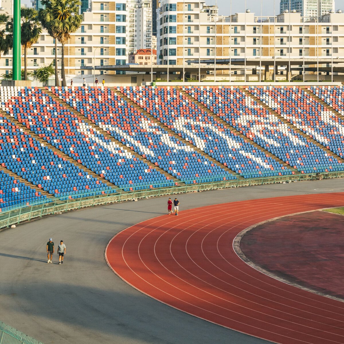 Curved running track and patterned grandstand at Phnom Penh’s Olympic Stadium, with walkers circling the venue.