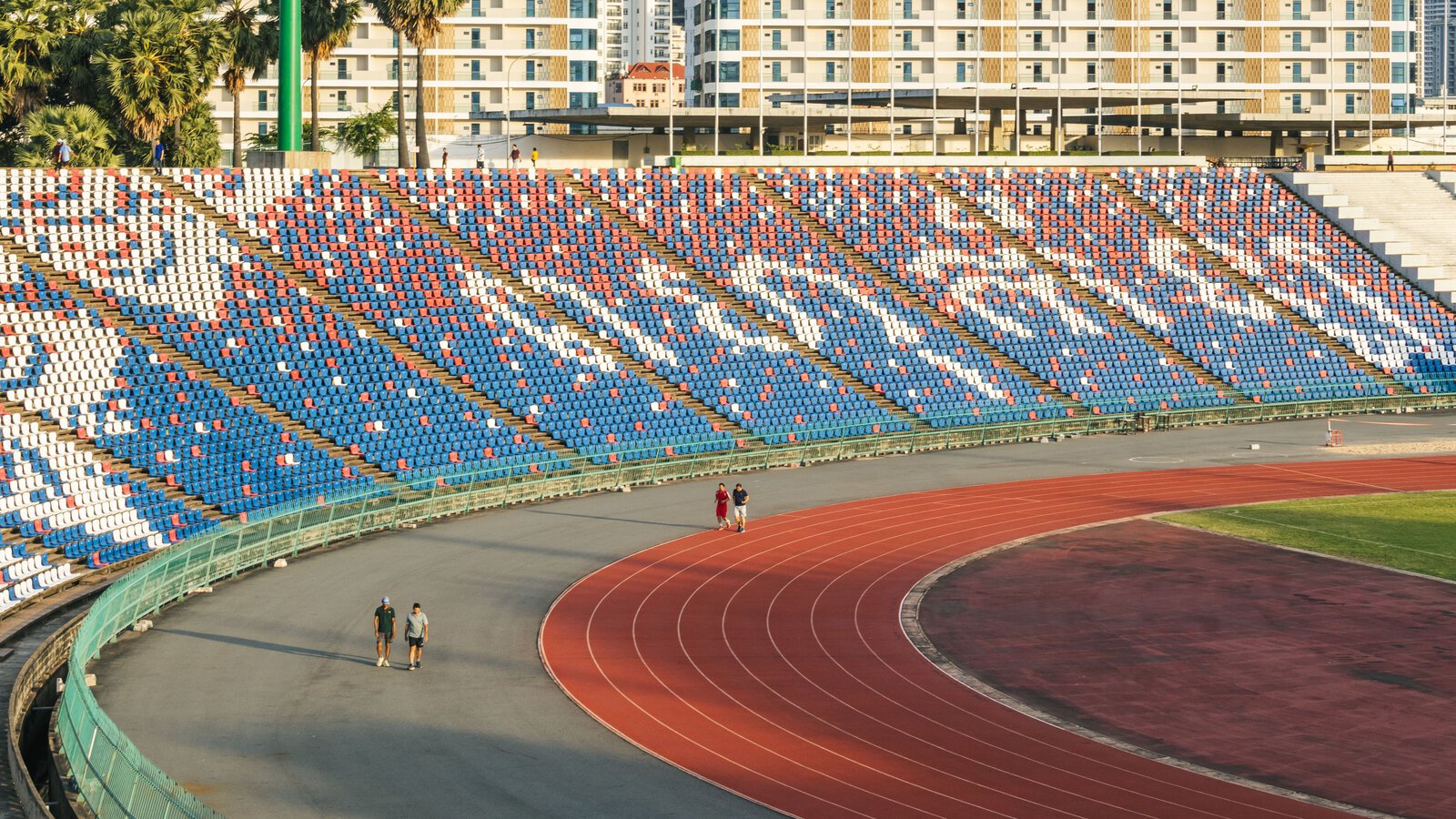 Curved running track and patterned grandstand at Phnom Penh’s Olympic Stadium, with walkers circling the venue.