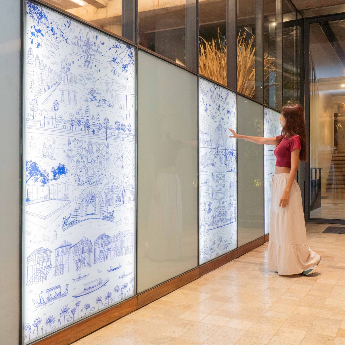 Visitor viewing illuminated illustrated panels depicting Cambodian landmarks, cultural scenes, and historical references inside Penh House Hotel.