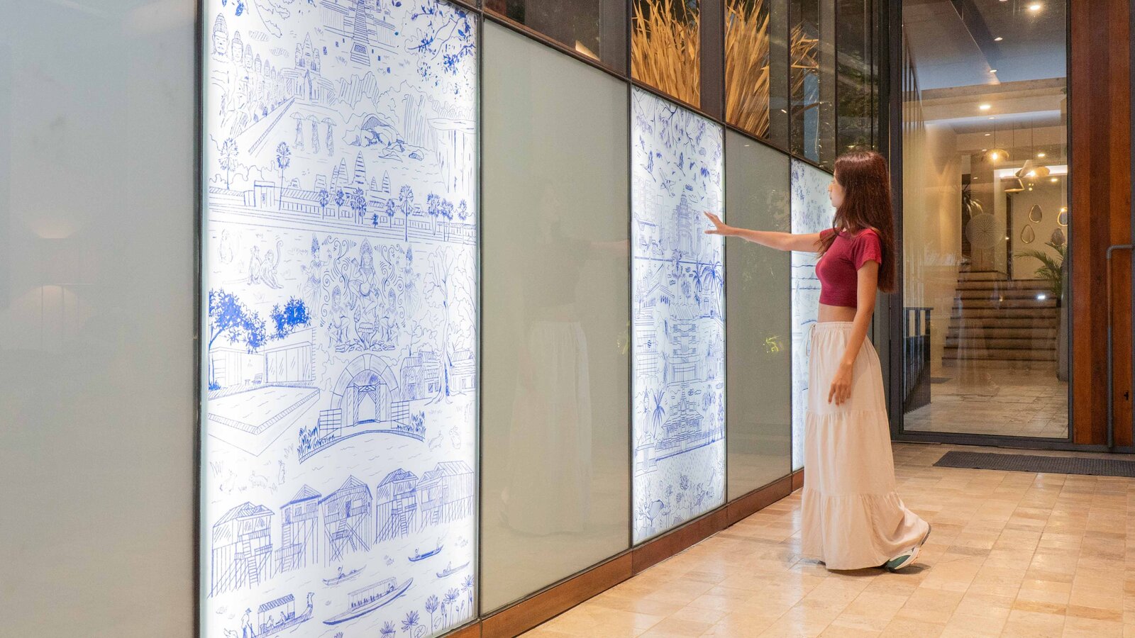 Visitor viewing illuminated illustrated panels depicting Cambodian landmarks, cultural scenes, and historical references inside Penh House Hotel.