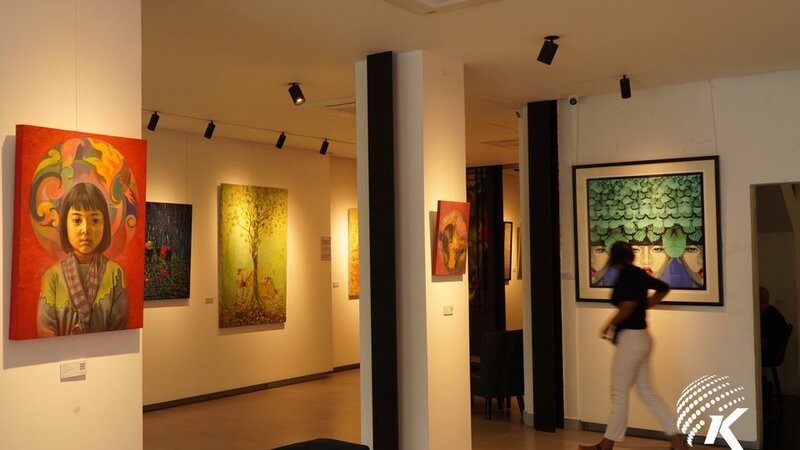 Visitor walks past bright, expressive portrait paintings hung on white walls inside a well-lit exhibition room.