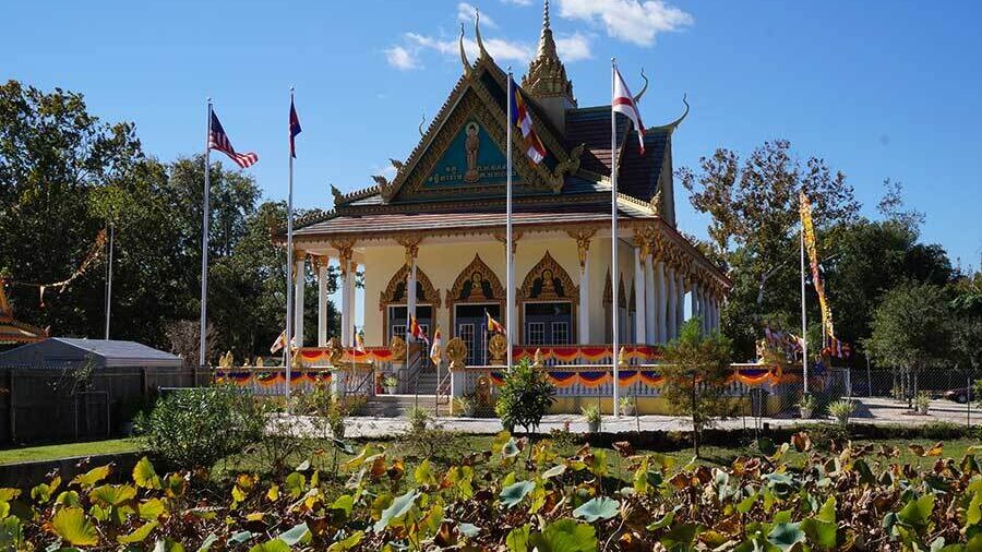 Temple architecture stands behind lotus ponds and ceremonial flags within the Cambodian Buddhist Center grounds.