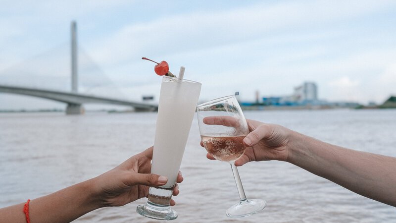 Two drinks raised beside the riverfront with a bridge in Phnom Penh.