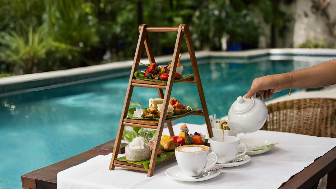 Tea poured beside an afternoon tea fusion set overlooking the pool.