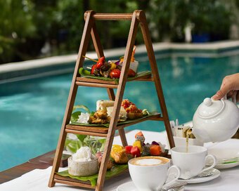 Tea poured beside an afternoon tea fusion set overlooking the pool.