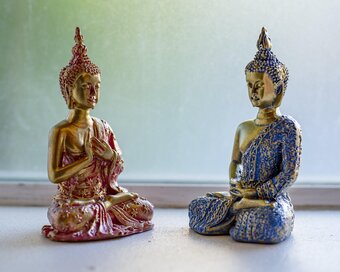 Two seated Buddha figurines in contrasting colours displayed on the window.