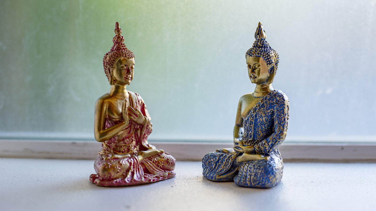 Two seated Buddha figurines in contrasting colours displayed on the window.