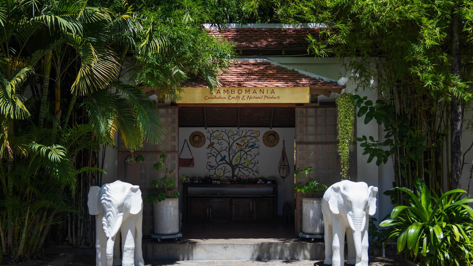 Entrance to Cambomania Shop by Pavilion Hotel framed by bamboo plantings and white elephant sculptures.
