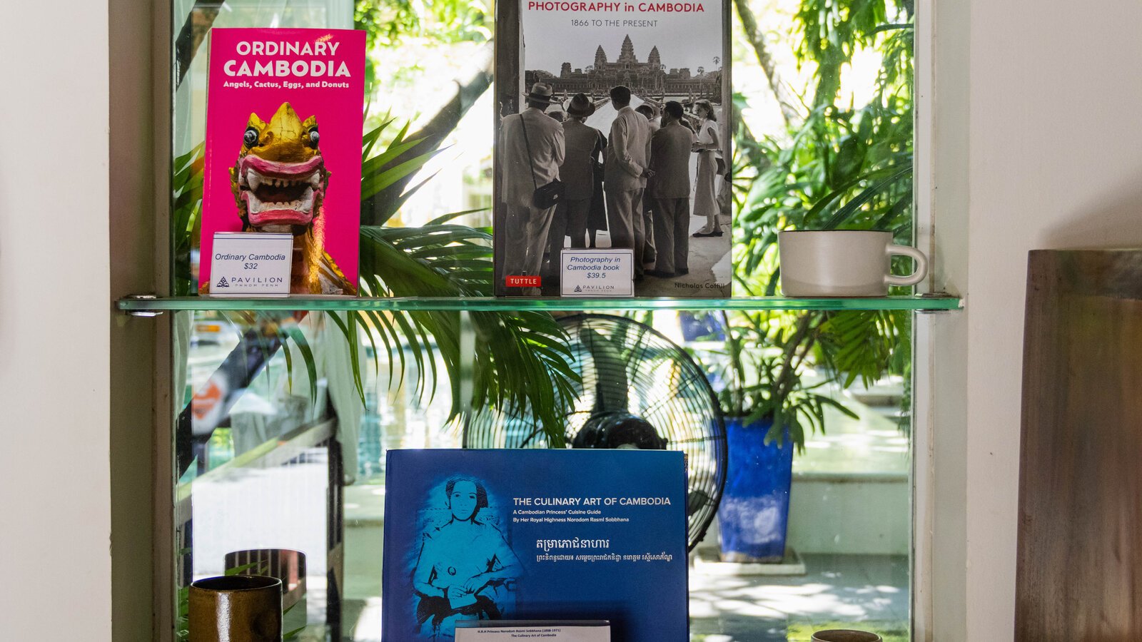 Selection of books featuring the Culinary Art of Cambodia by HRH Princess Norodom Rasmi Sobbhana (augmented edition), Photography in Cambodia: 1886 to the Present, by Nicholas Coffill, arranged on a display shelf.
