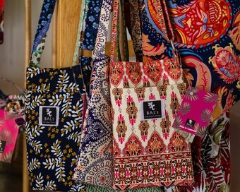 Collection of patterned fabric handbags made in Cambodia, hanging on a wooden display rack.