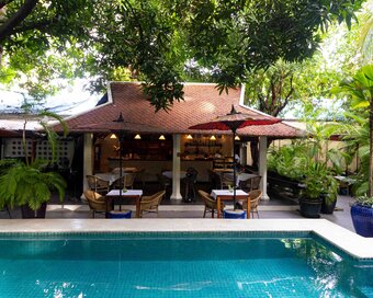 Open-air restaurant with traditional roof, surrounded by trees and plants by the pool.