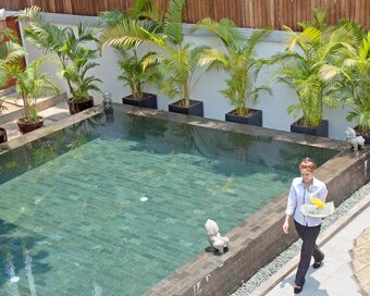Pavilion service team member carries refreshments by the Sun Pool walkway lined with palms and stone details.