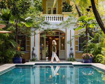Guest walking in front of Pavilion’s Lush Pool and old house heritage building.