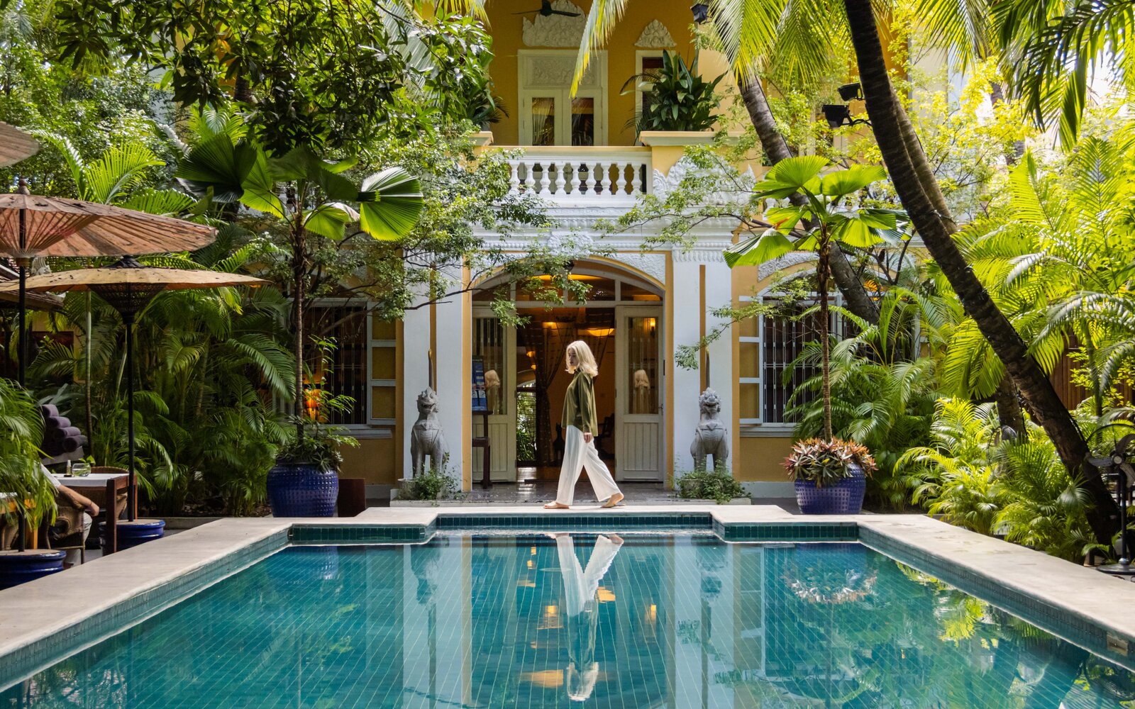 Guest walking in front of Pavilion’s Lush Pool and old house heritage building.