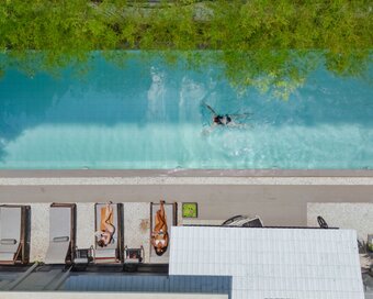 Guests lying on poolside loungers next to a guest gliding through the lap pool of White Mansion Hotel, Phnom Penh