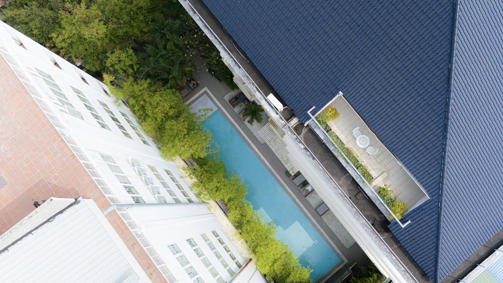 Aerial shot looking down at the roof of White Mansion and the lap pool between the building and lush green trees.