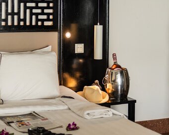 White Mansion hotel bed styled with a magazine, camera, and straw hat next to a bedside bucket of chilled wine.