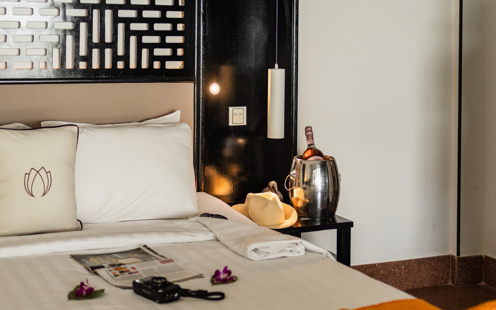 White Mansion hotel bed styled with a magazine, camera, and straw hat next to a bedside bucket of chilled wine.