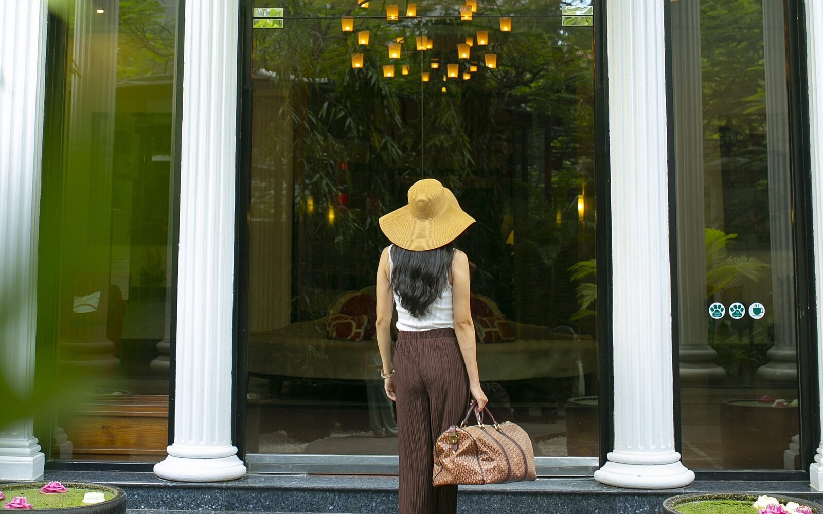 Guest carrying a travel bag walks up the steps toward the hotel's glass doors of White Mansion, Phnom Penh