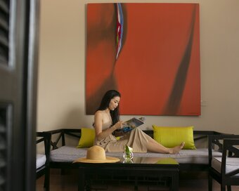 Guest sitting on a sofa bed reading a magazine beneath a large red painting at White Mansion, Phnom Penh