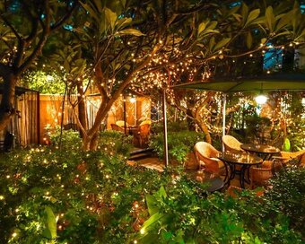Outdoor café tables and woven chairs lit up by warm fairy lights in a leafy garden at Le Café, White Mansion, Phnom Penh