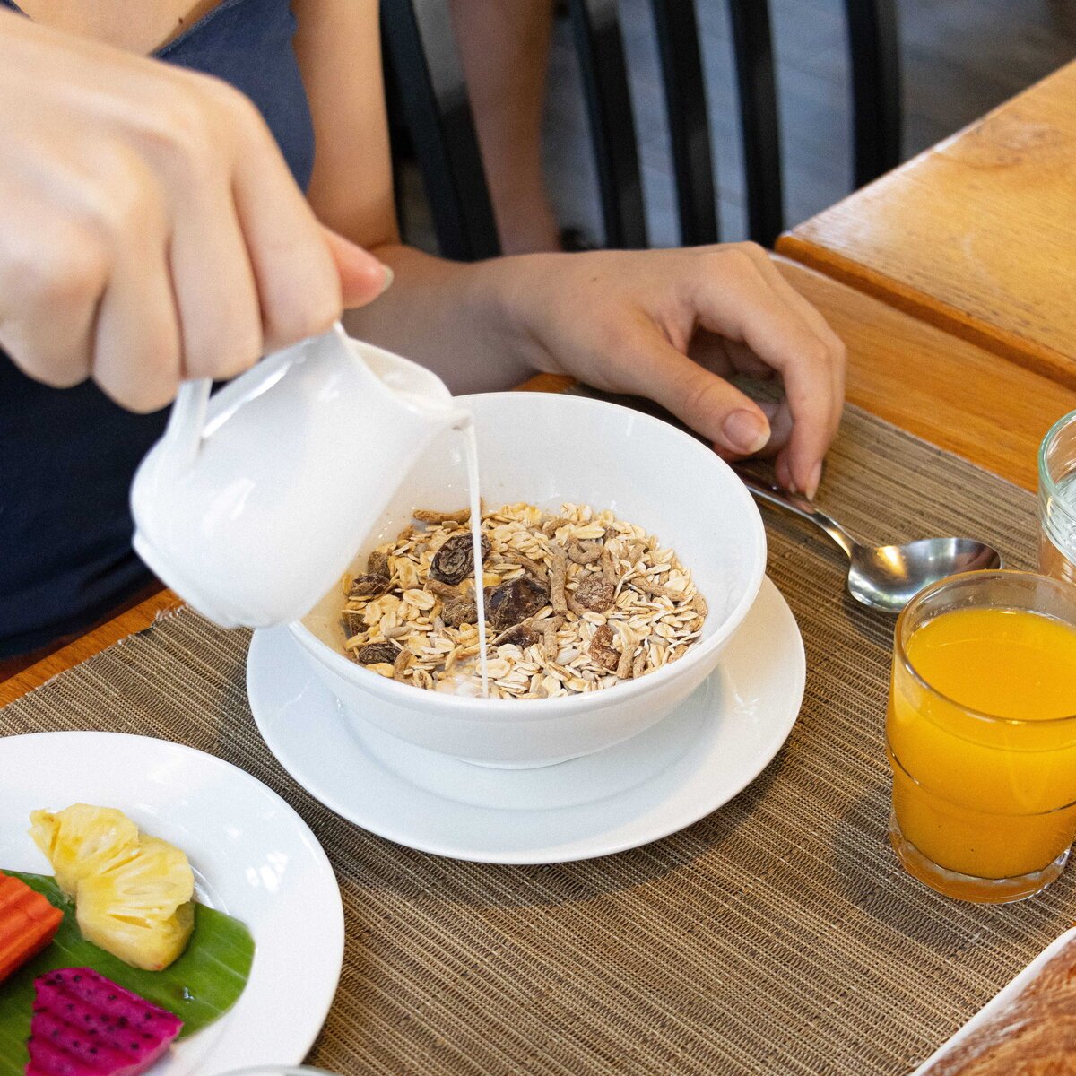 Hand pouring milk into a white bowl of cereal at Le Café, White Mansion Hotel, Phnom Penh.
