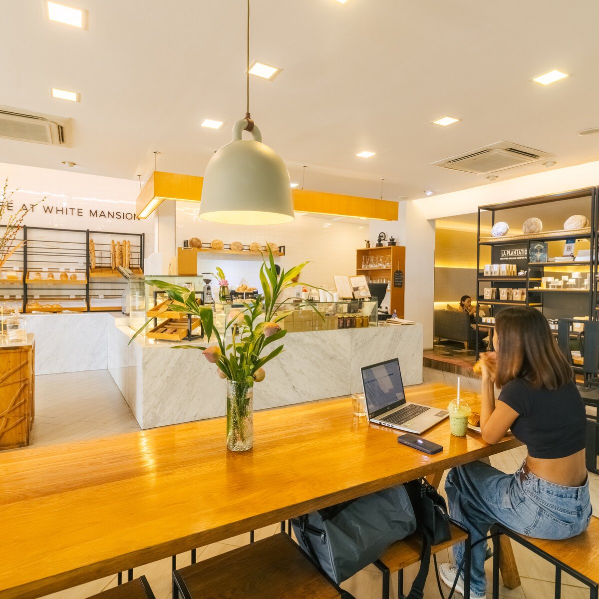 Guest sitting with a laptop at a long wooden table at Le Café, White Mansion, Phnom Penh